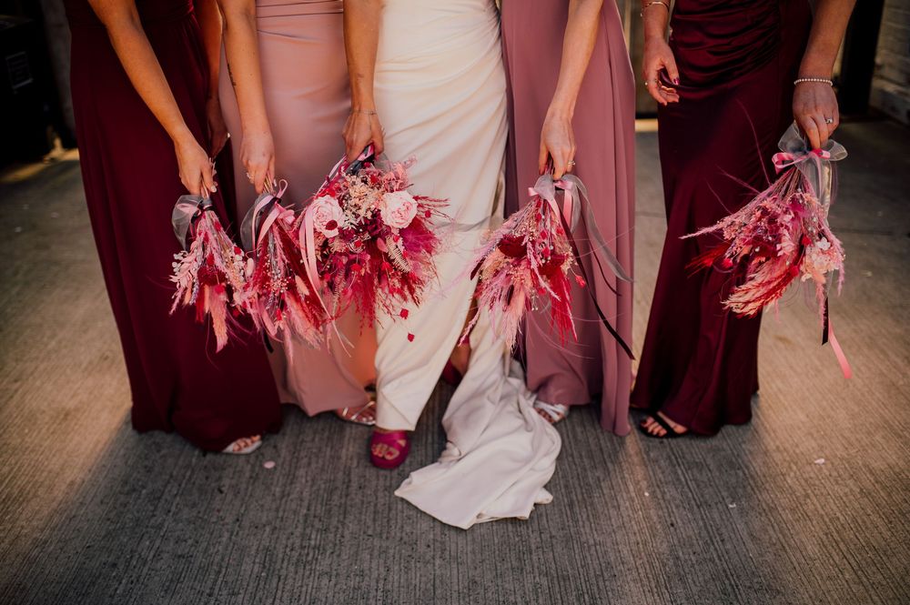 A row of bridesmaids in burgundy and pink dresses walk together showing the flowing skirts of their gowns.