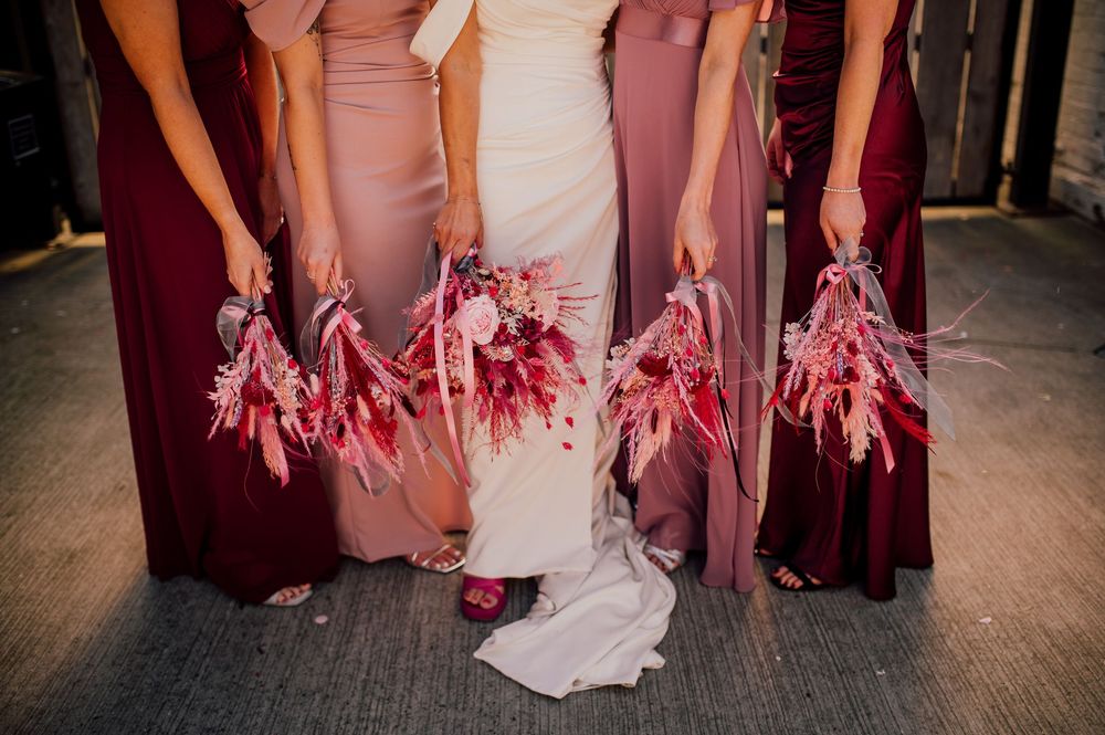 Wedding party members show off their shoes in a fun group photo on a wooden floor.