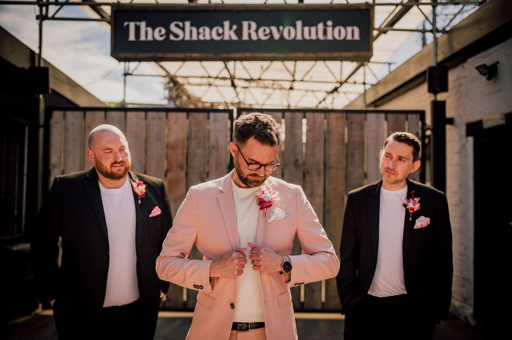 Groomsmen share joyful reactions during a rustic barn wedding celebration.