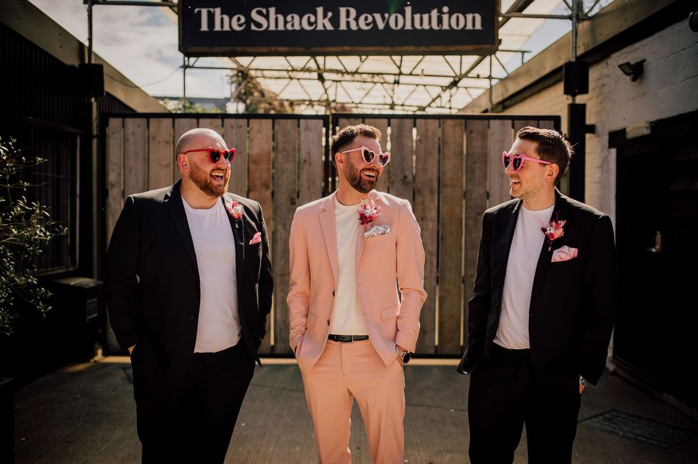 A series of wedding party photos showing people in black suits and pink attire posing against various outdoor backgrounds.