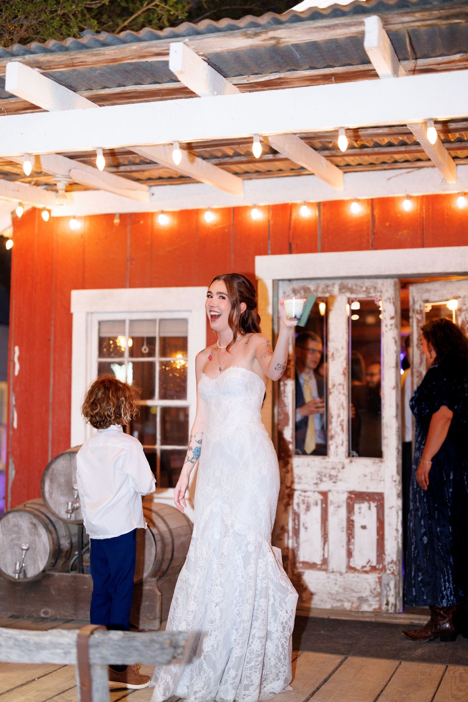 Wedding guests dance and celebrate under a rustic covered patio with string lights creating a warm, festive atmosphere.