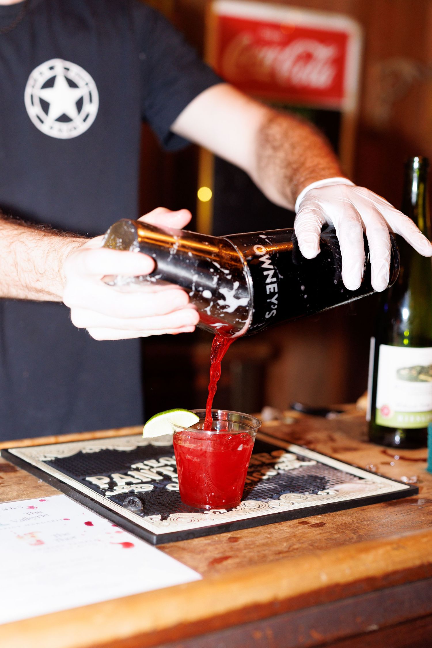 A series of hands pouring red cocktails into glasses on a dark wooden bar counter.