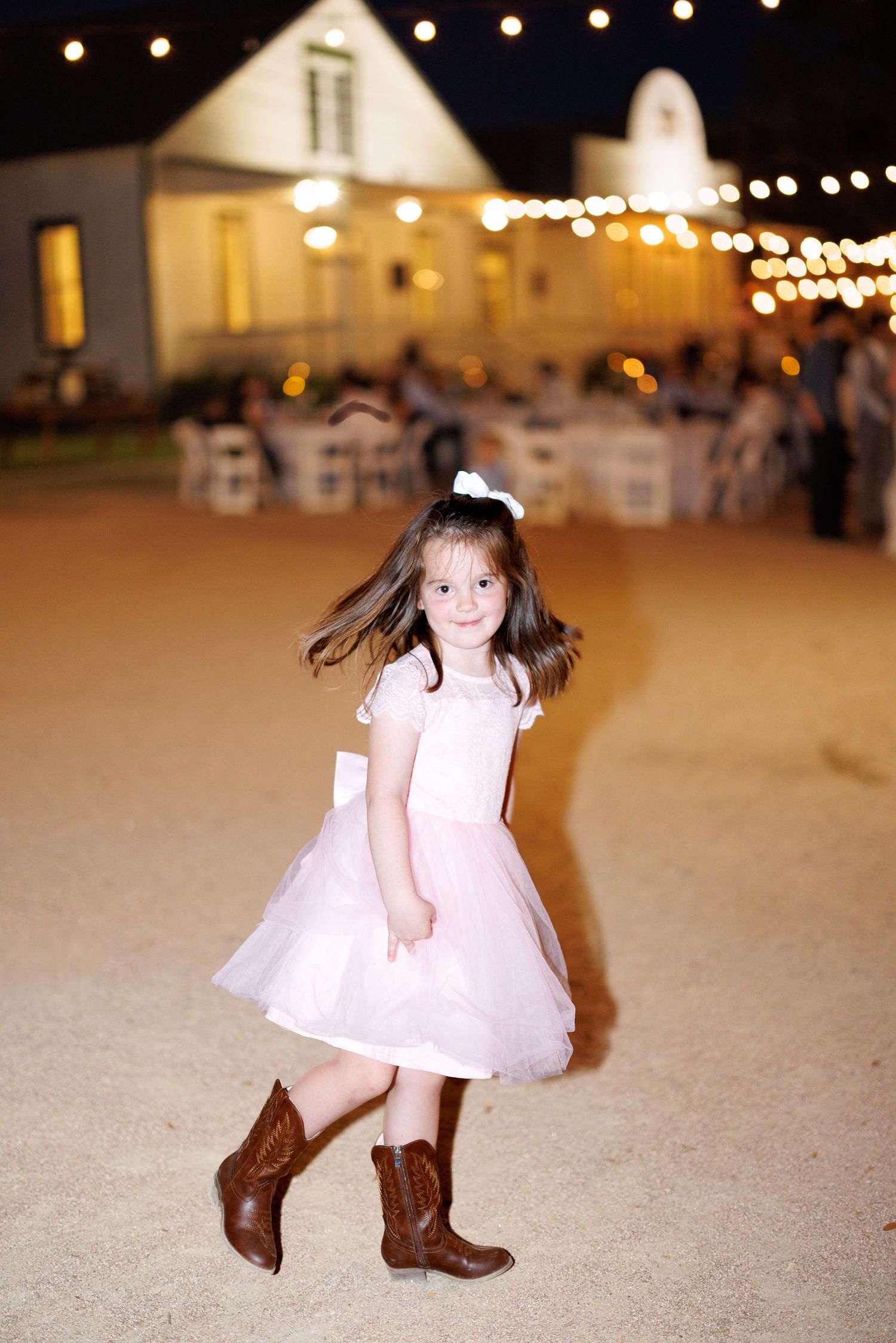 A sequence of photos showing a small figure in a white dress and cowboy boots twirling and dancing on a paved surface at night.