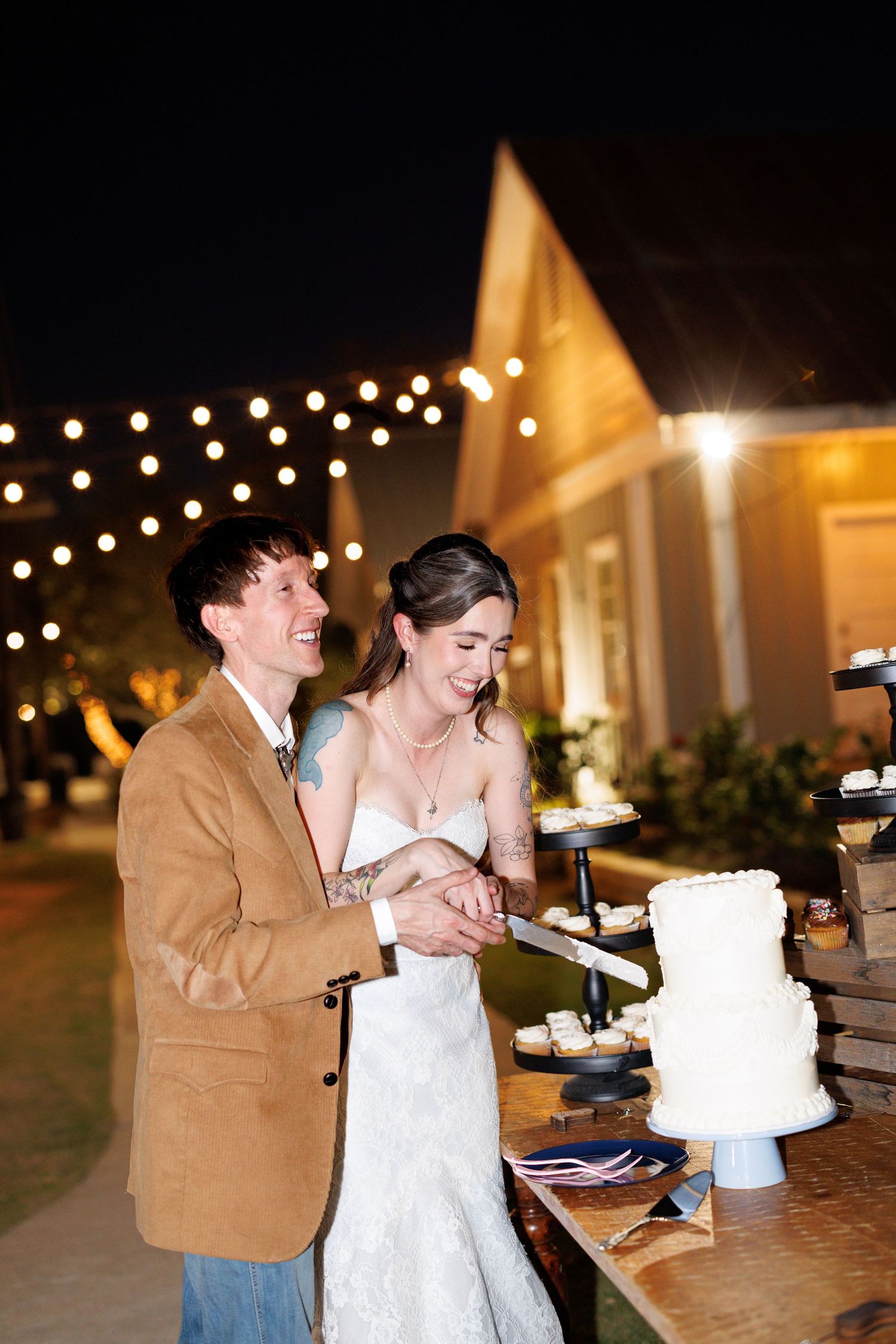 Wedding couple sharing cake at reception with string lights in background.