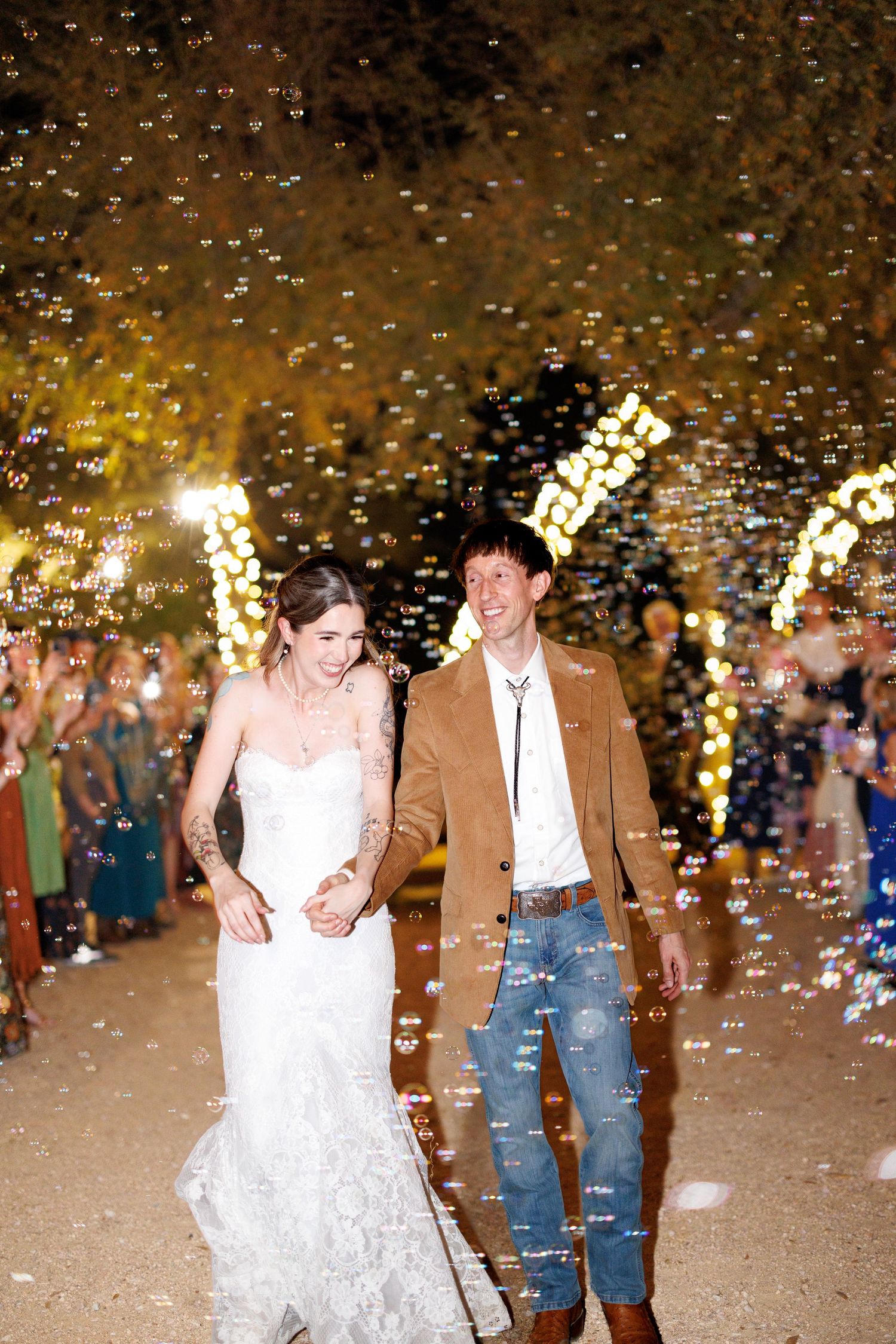 Newlyweds walking through shower of bubbles during evening celebration.