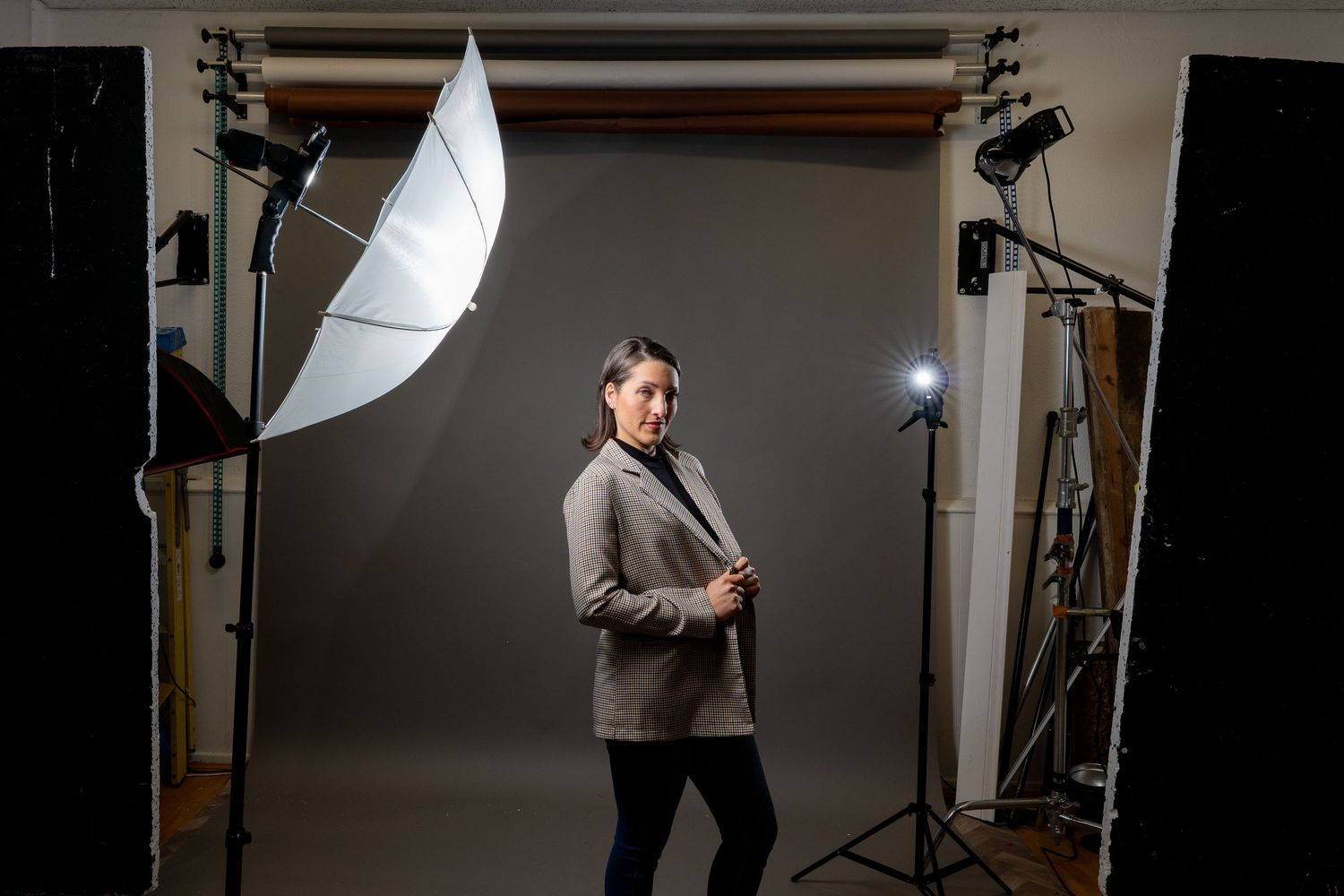 Professional photography studio setup with lighting equipment, umbrellas, and stands against a gray backdrop.