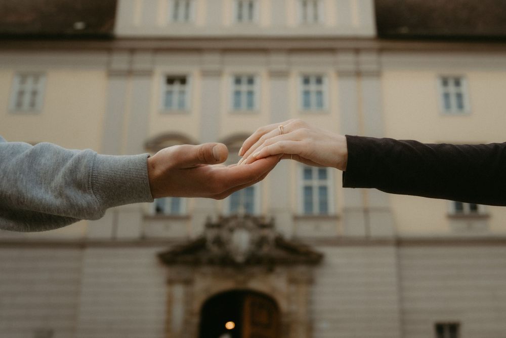 Two hands reaching towards each other against a blurred architectural background in a dramatic gesture.