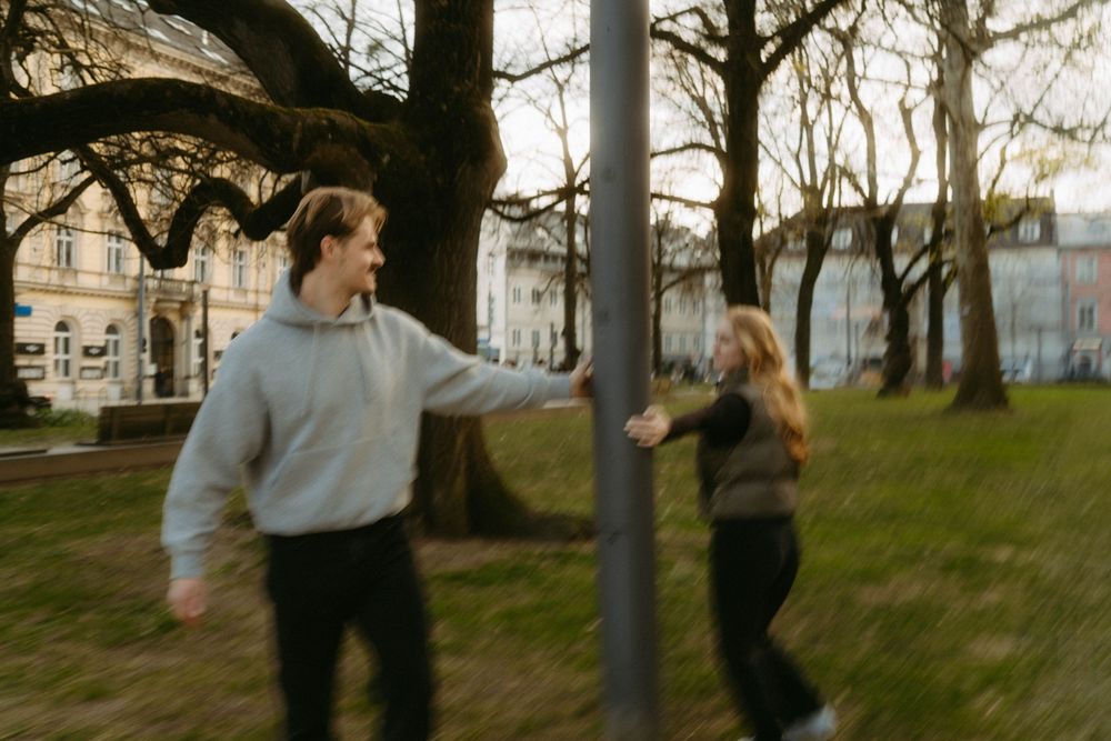 Two people walking through a park with bare trees and lamp posts on an overcast day.