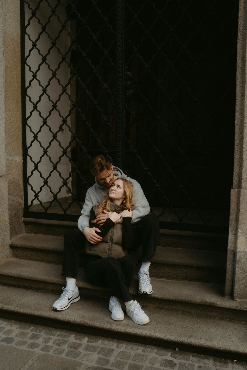 A moody series showing an intimate moment between two people sitting by an ornate window frame.
