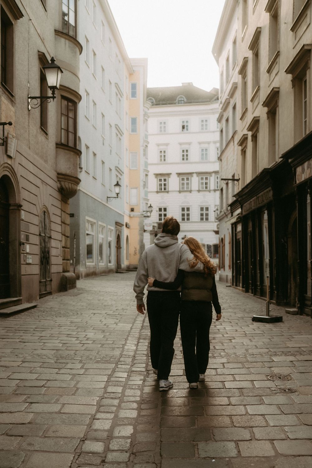 A couple walks together down a charming cobblestone street in a historic European city district.