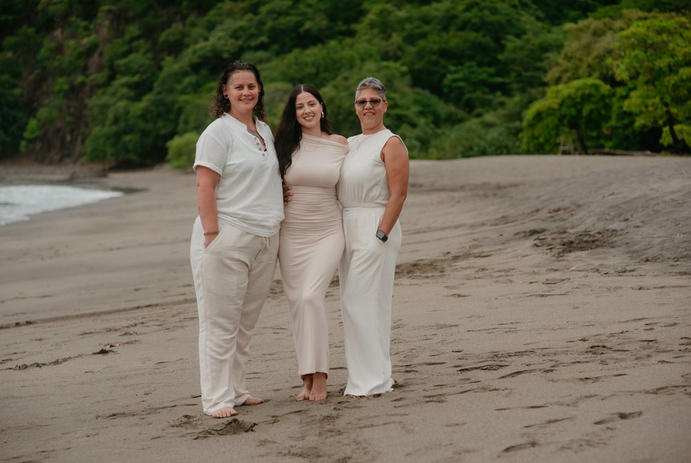 Family members wearing coordinated white and beige outfits walk together on a sandy beach at sunset.