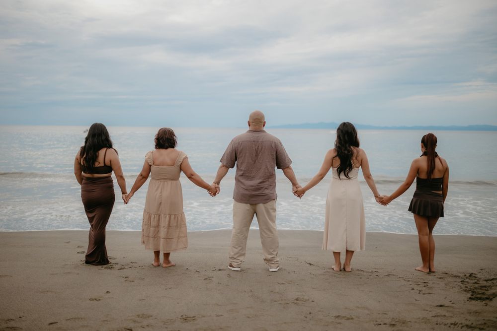 A group of people holding hands while standing on a beach at sunset with the ocean in the background.