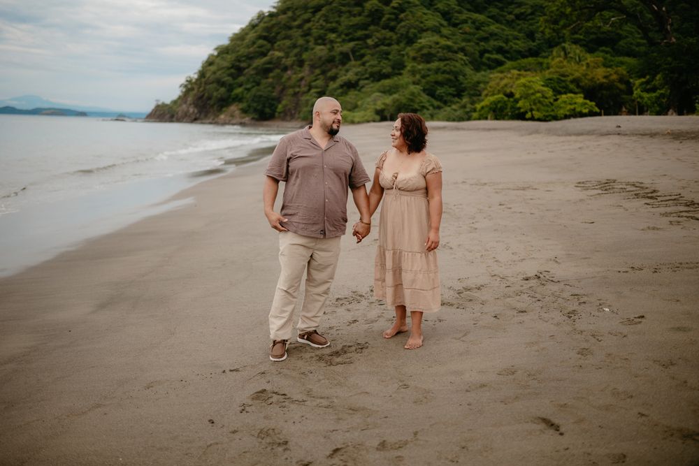 Two people in coordinated outfits walking hand in hand along a scenic beach with cliffs and ocean views.