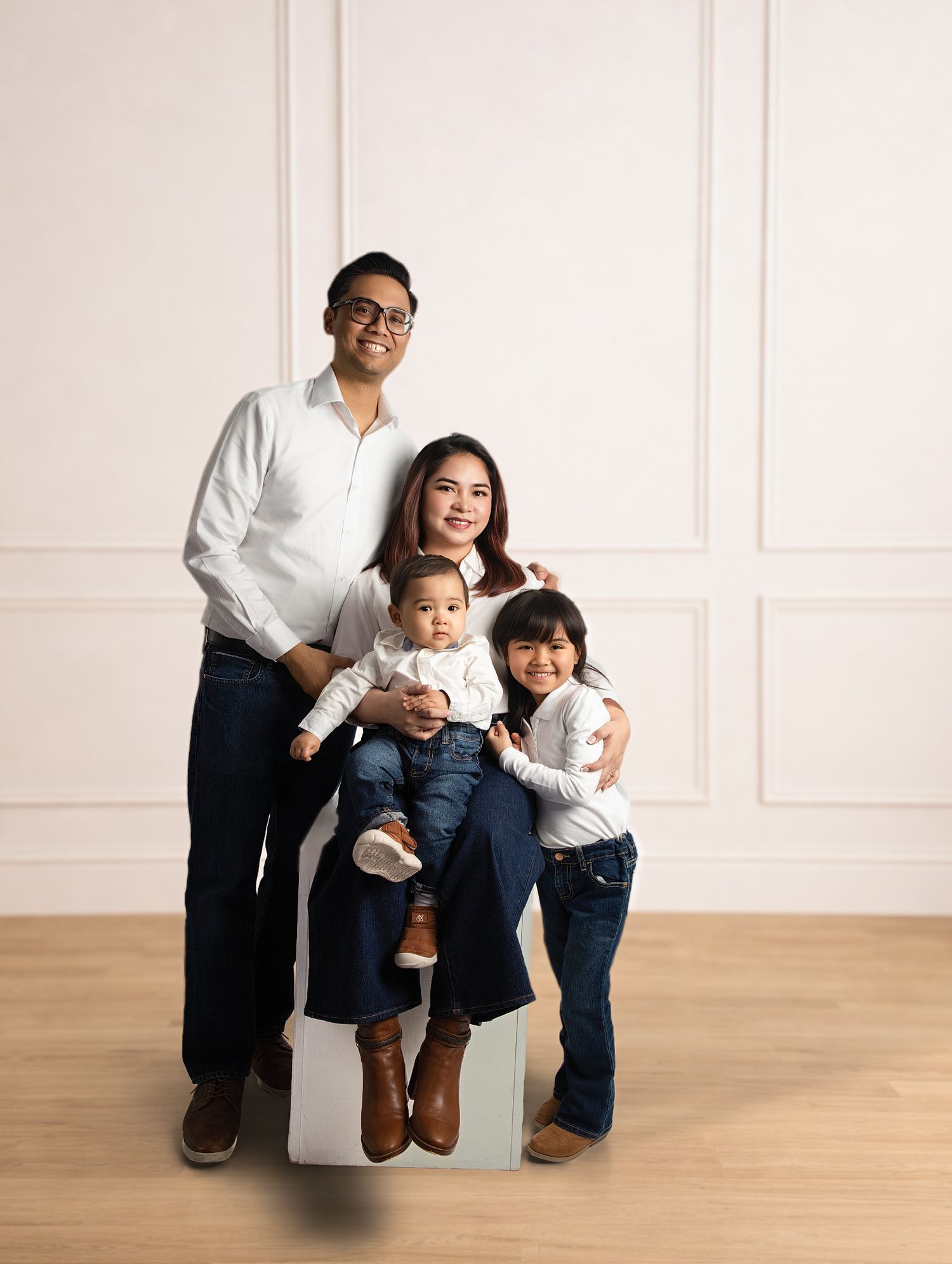 Asian family of four posing in white studio, parents in white shirts and jeans with two young children.