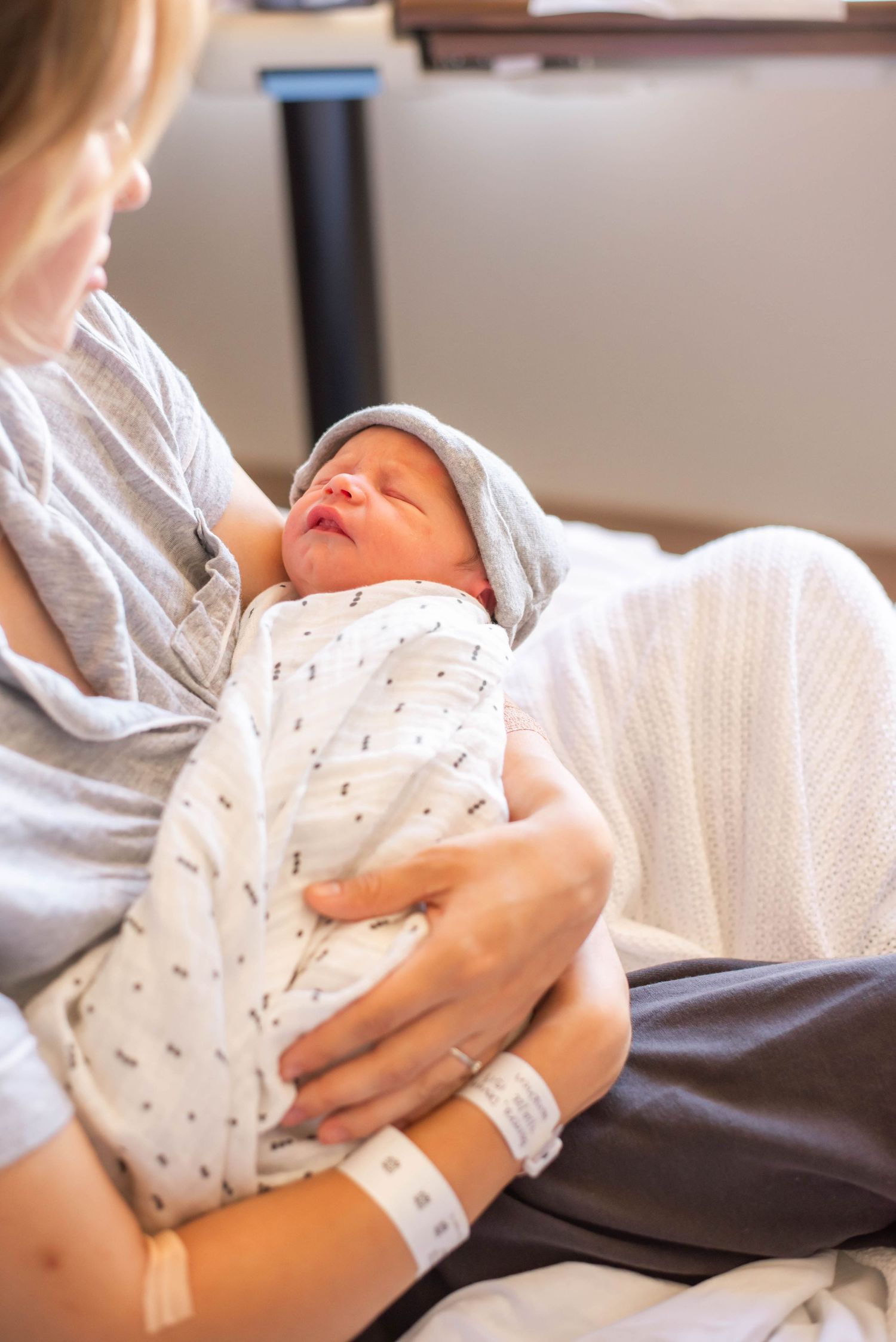Mother holding swaddled newborn baby in hospital room after delivery.