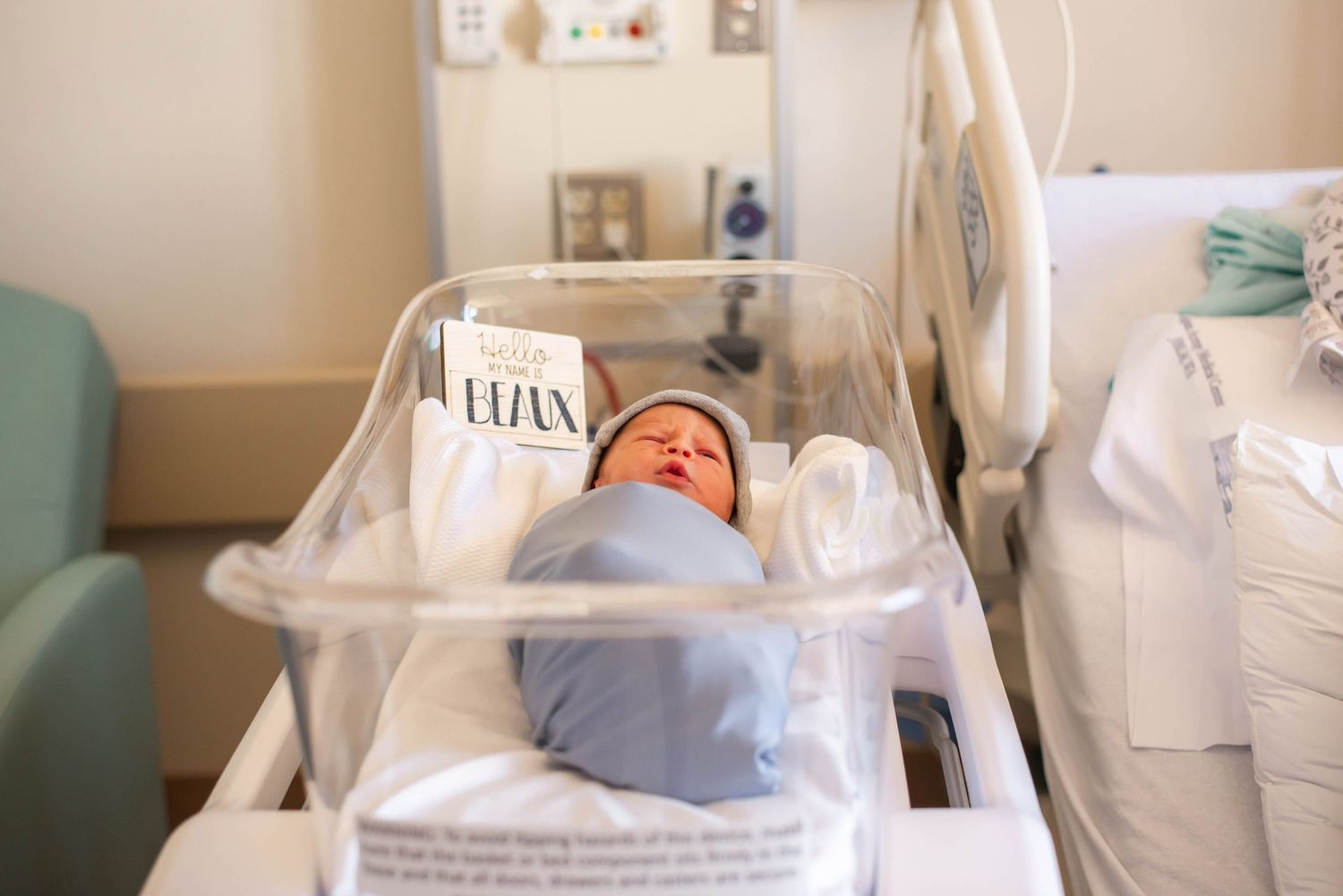Newborn baby swaddled in blue blanket resting in hospital bassinet with name card, peaceful maternity ward setting.
