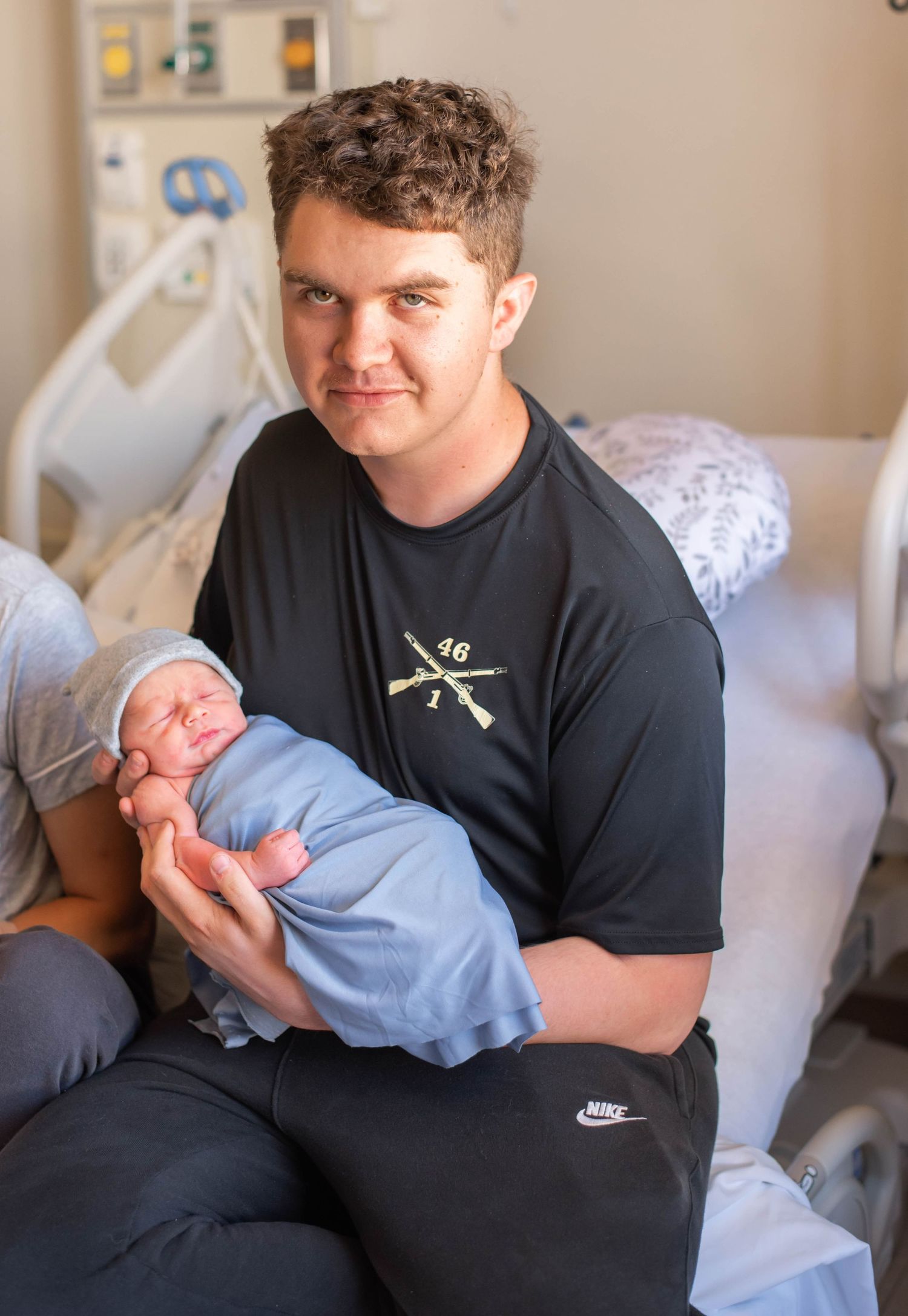Young father holding swaddled newborn baby in blue blanket at hospital after birth.