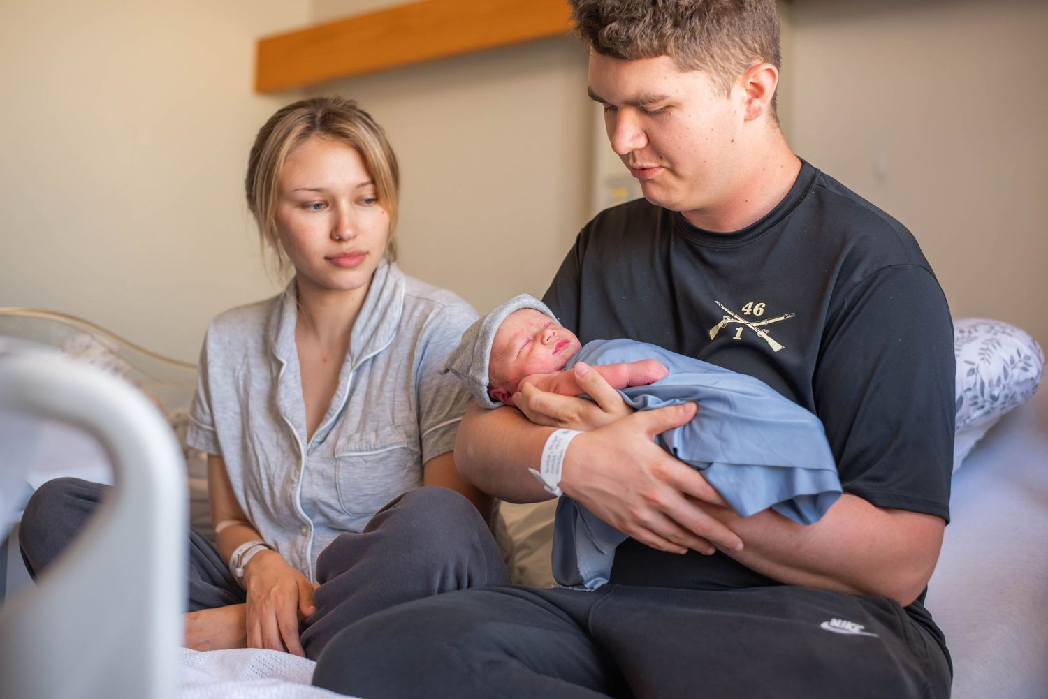 New parents holding their swaddled newborn baby together in hospital room after birth.