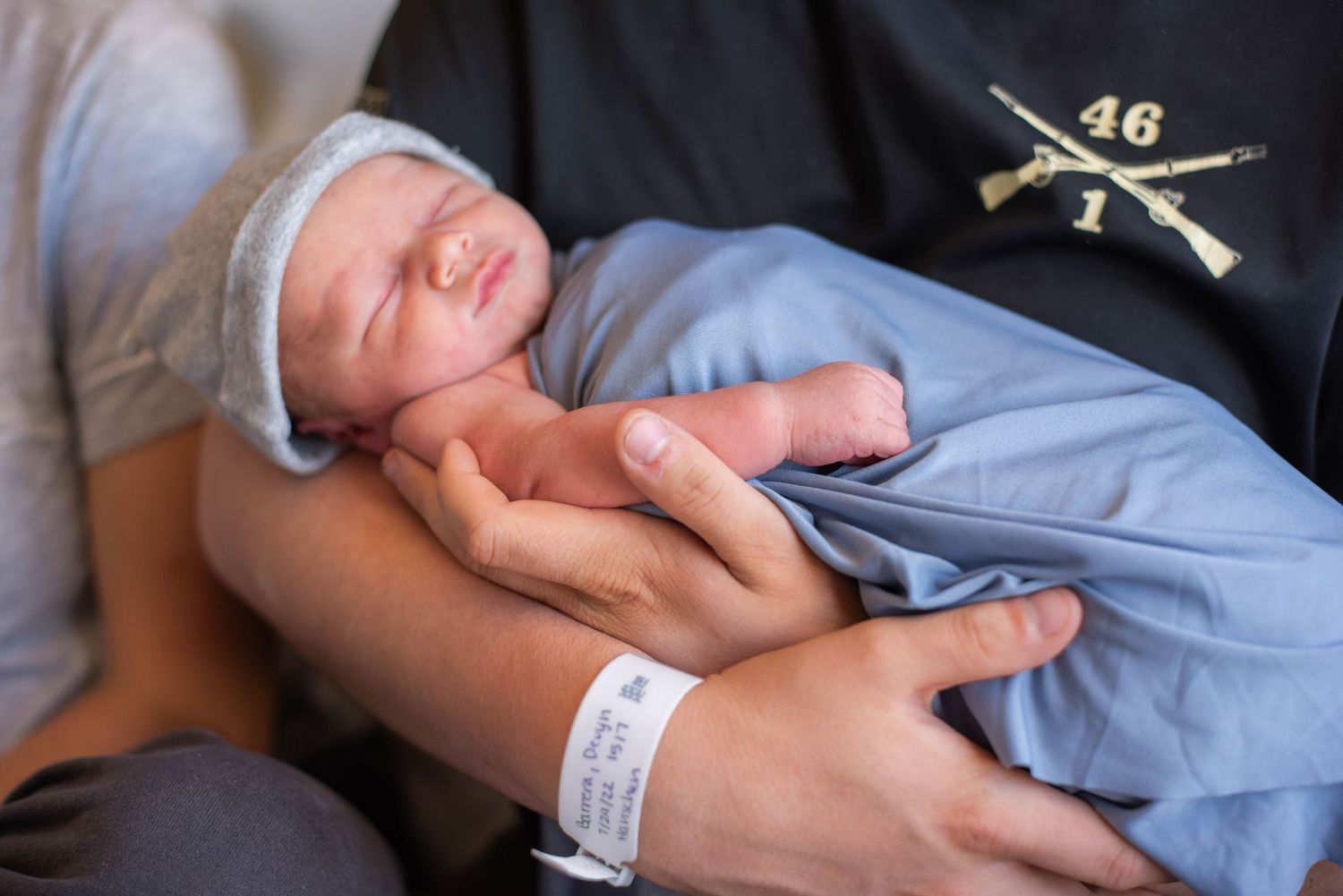 Close-up of newborn baby swaddled in blue blanket being cradled in fathers hands at hospital.