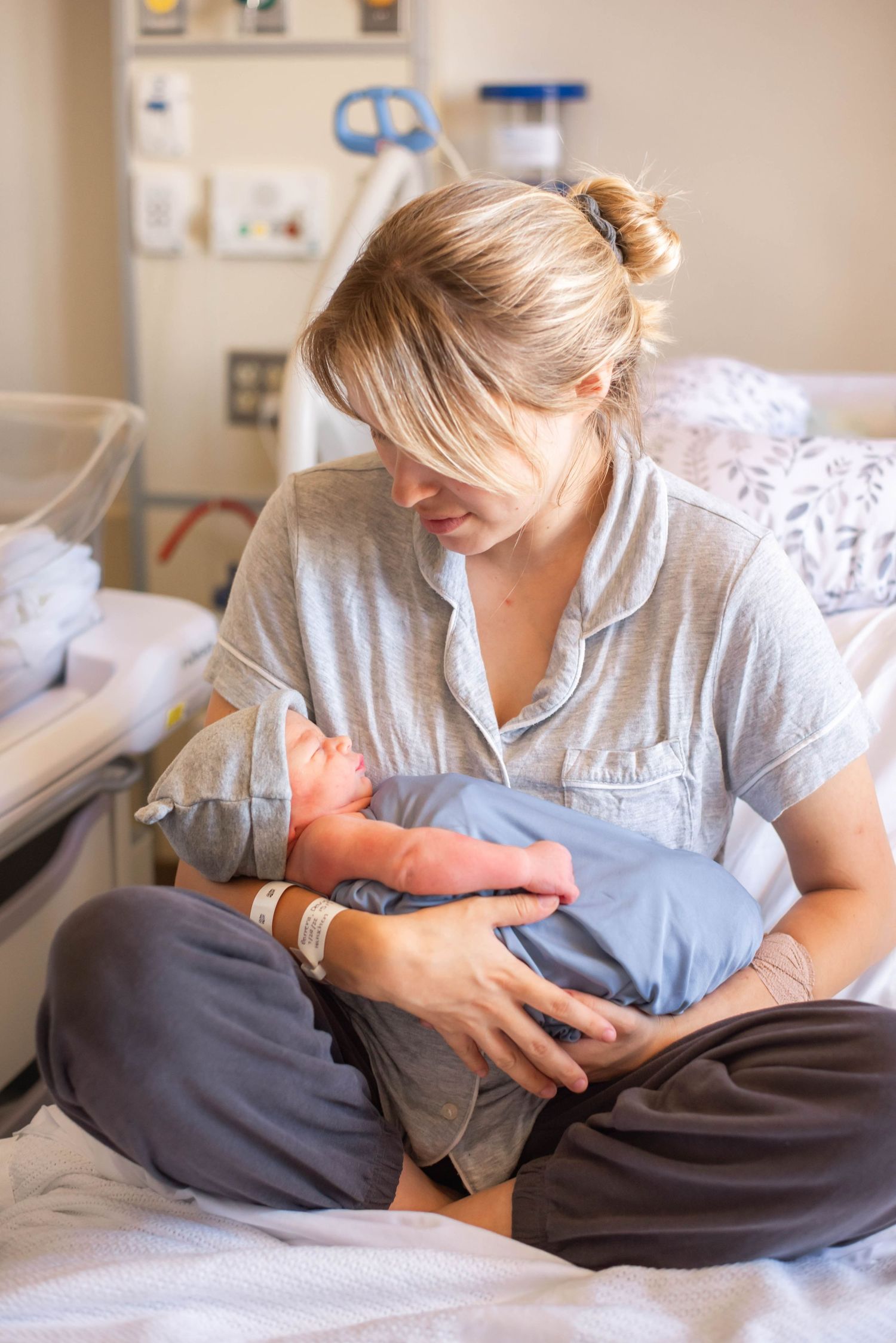 New mother sitting on hospital bed cradling her newborn baby in arms.