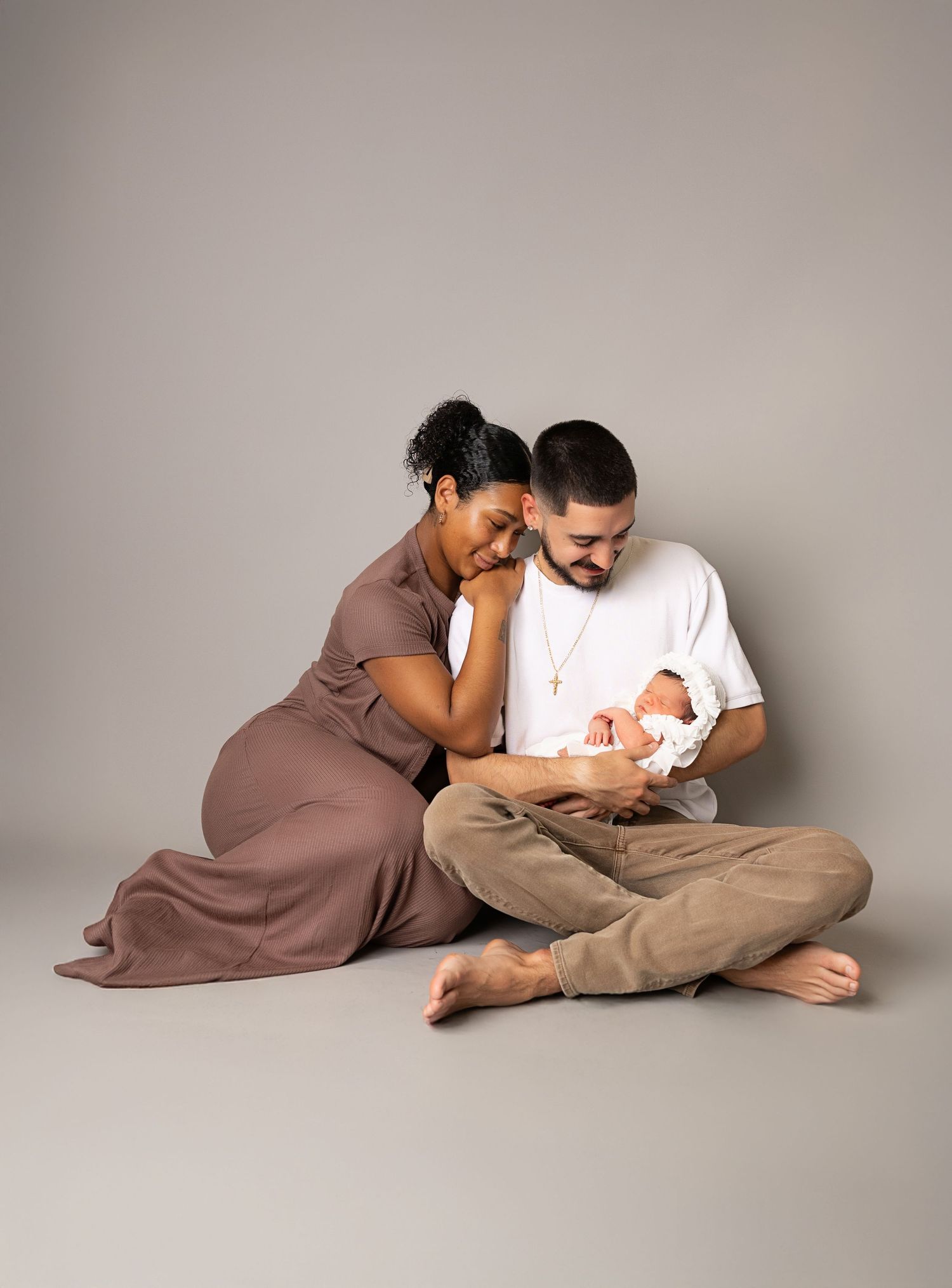 A couple sits on the floor gazing lovingly at their newborn baby during a professional studio portrait session.