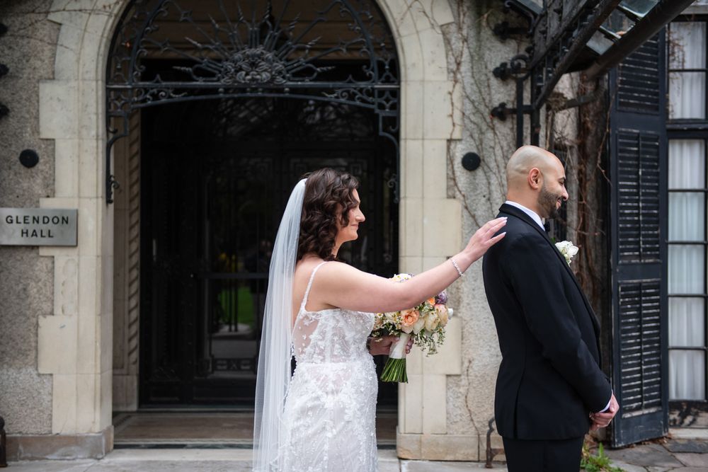 Bride taps groom's shoulder for first look reveal outside Glendon Hall entrance.
