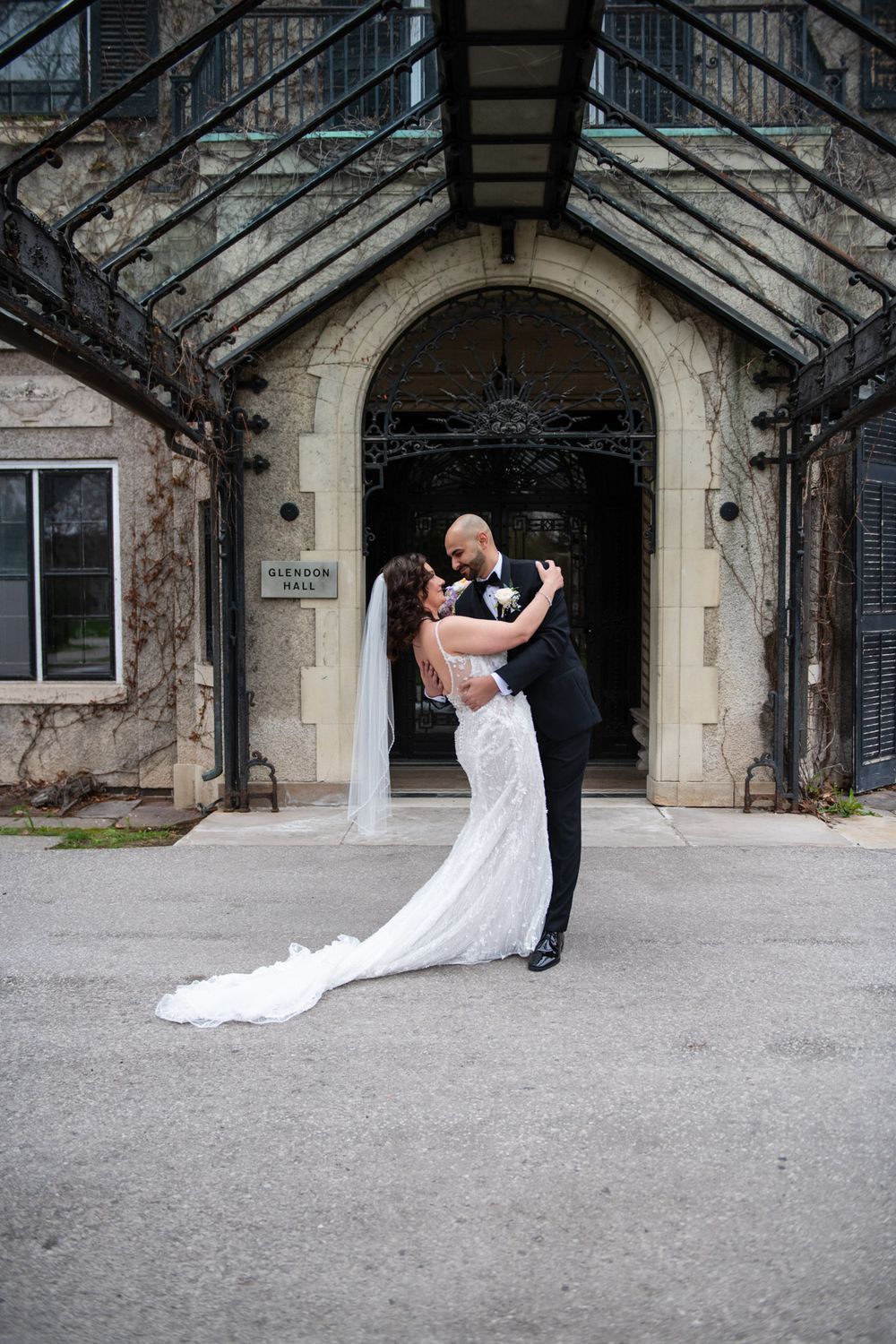 Bride and groom share romantic embrace outside Glendon Hall stone archway entrance.