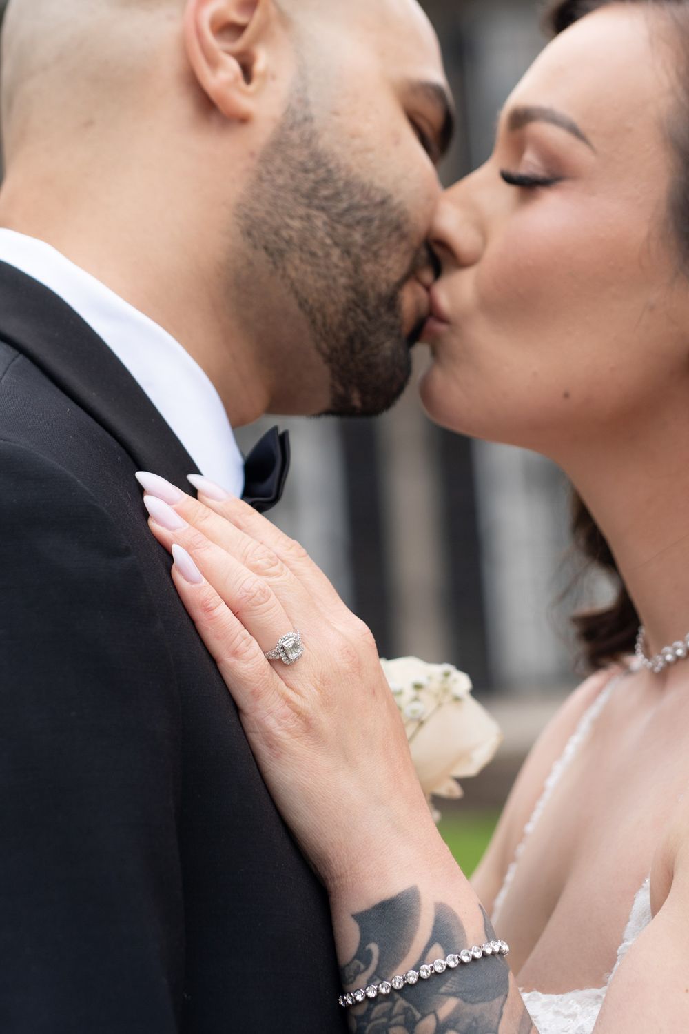 Close-up of bride and groom kissing, showcasing diamond engagement ring and tattooed hand.
