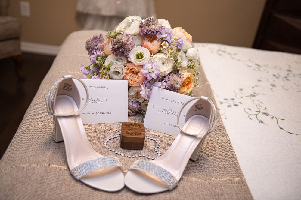 Wedding flat lay featuring glittery heels, floral bouquet, rings, and invitation cards on a table.
