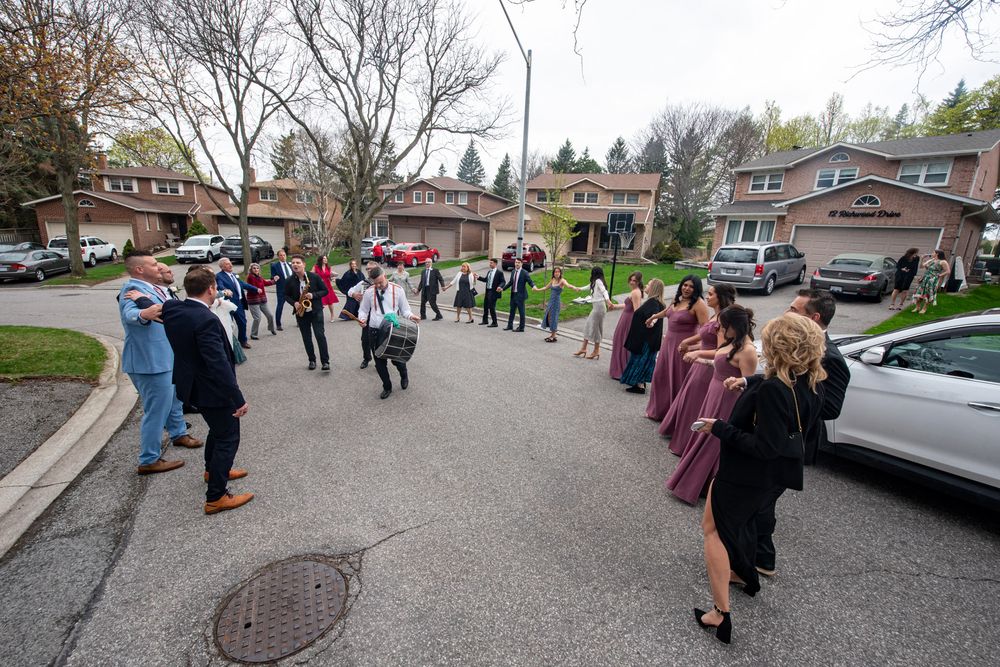 Wedding party and guests line the street cheering as the bride and groom arrive home.