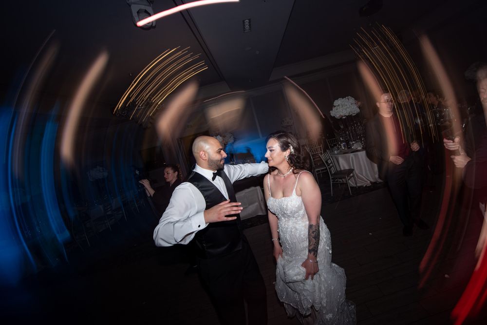 Bride and groom share a romantic dance on the wedding reception dance floor under colorful lights.