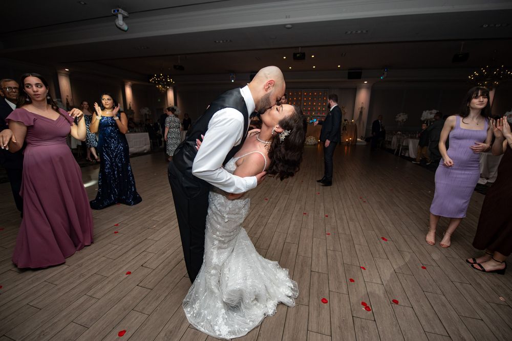Groom dips bride in a romantic first dance surrounded by guests on rose petal-covered dance floor.