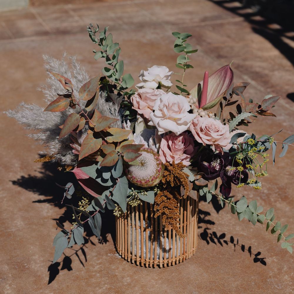 Romantic boho wedding bouquet with blush roses, protea, and eucalyptus in a gold ribbed vase.