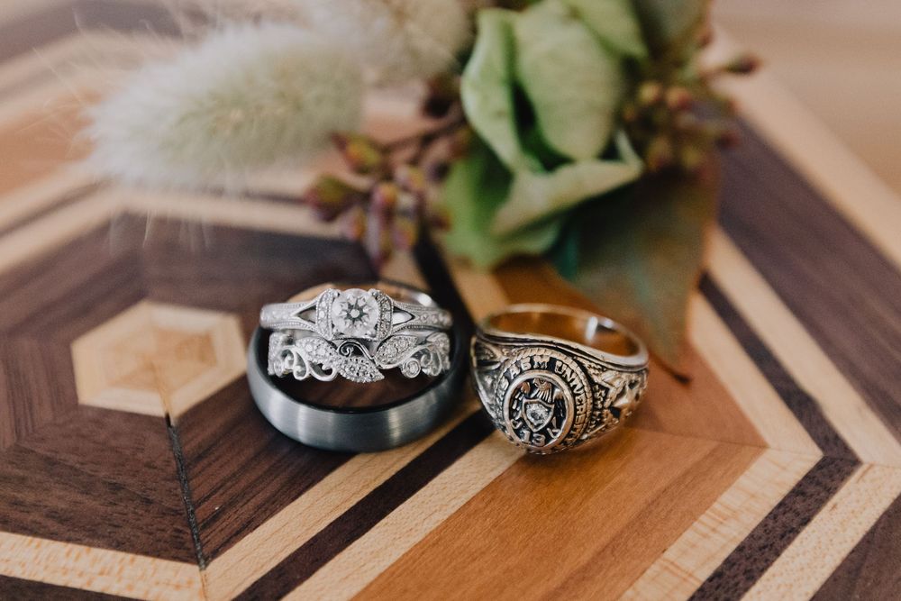 Three wedding rings displayed on a wooden surface, including a diamond engagement ring and signet ring.