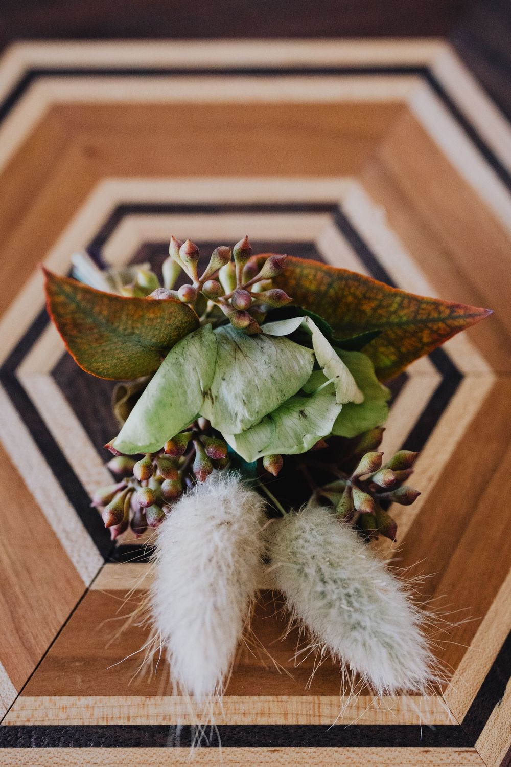 Elegant wedding boutonniere with succulents, green leaves, and fluffy bunny tail grass on geometric wood tray.