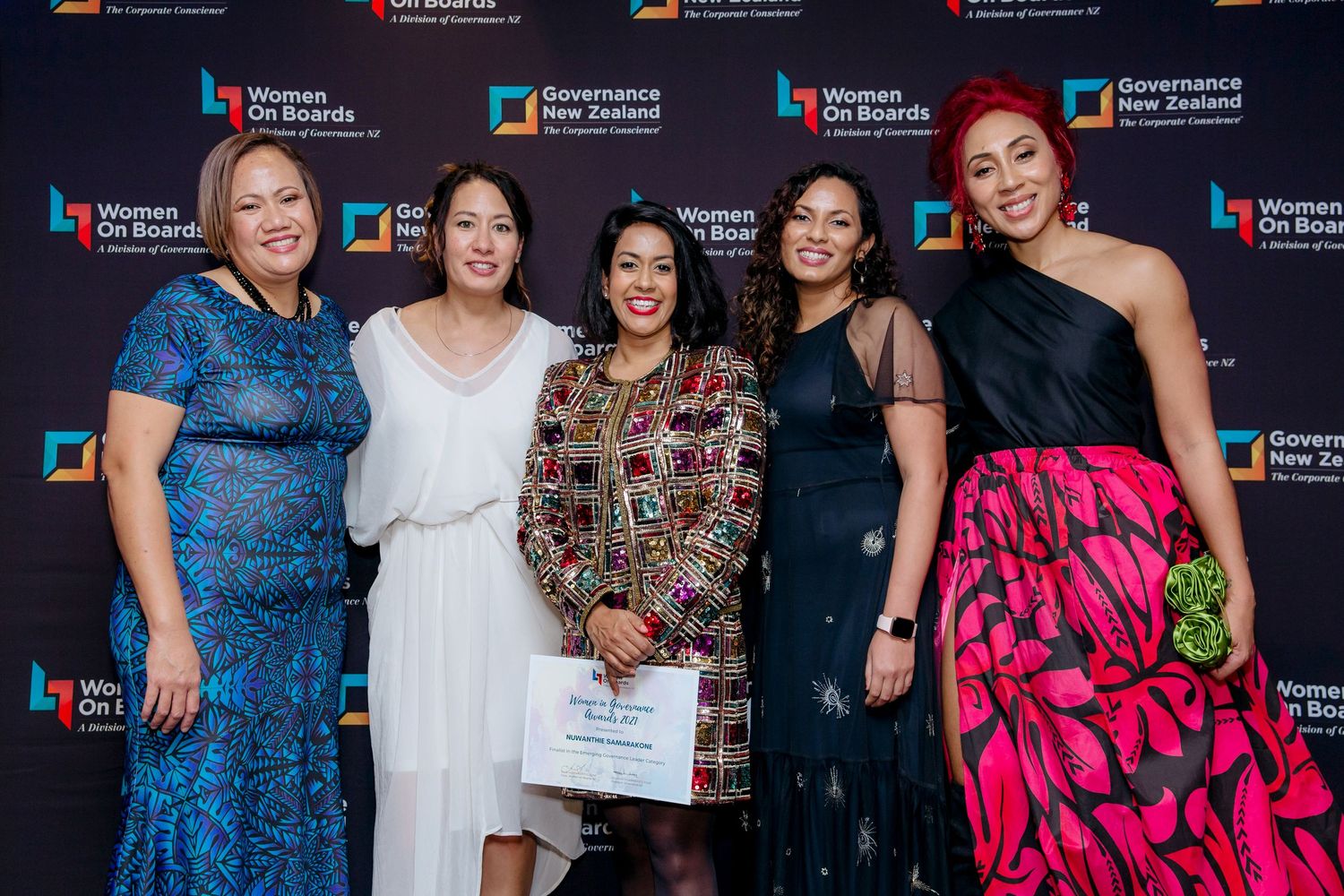 Five women at a corporate event standing in front of a media wall with the certificate they were awarded