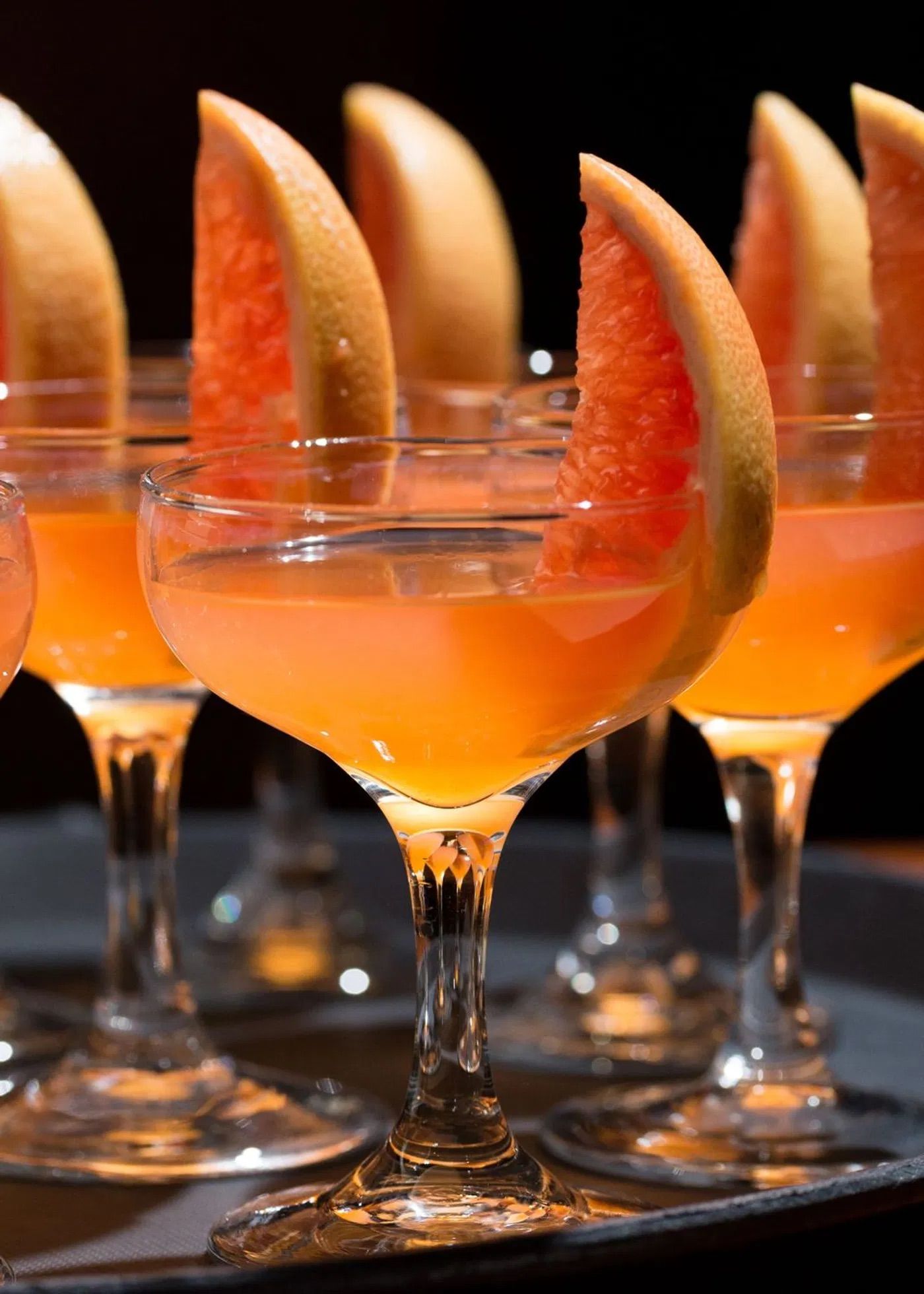 Glasses filled with a vibrant orange cocktail garnished with slices of citrus fruit.
