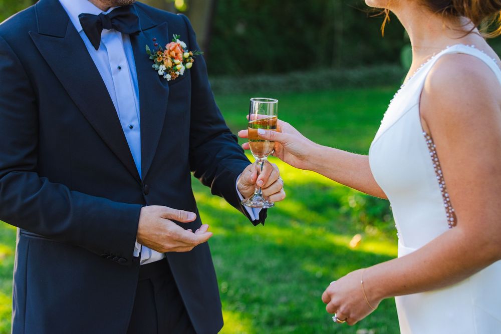 A man in a suit and a woman in a wedding dress stand together, holding a glass of champagne.