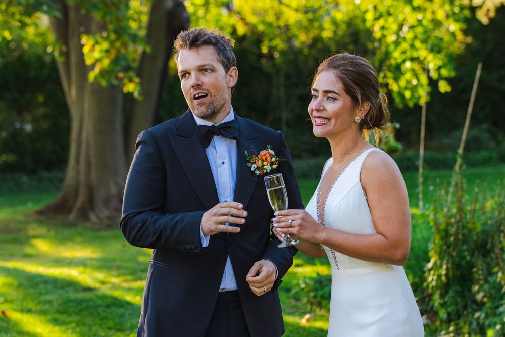A happy couple in formal attire standing together and smiling, holding champagne glasses.
