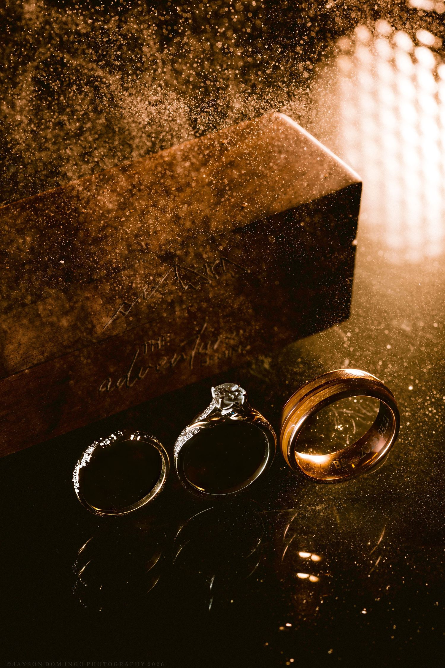 Three wedding rings displayed beside a rustic golden box with elegant bokeh lighting.