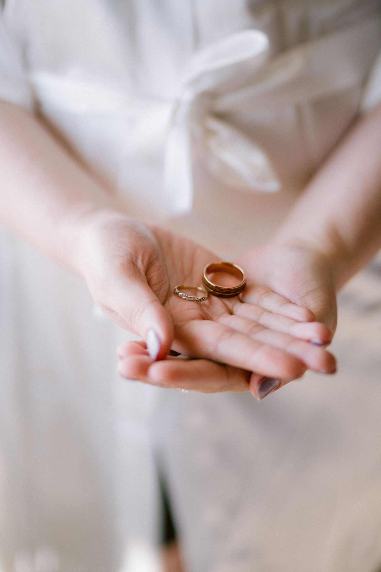 Person in white dress holding two gold wedding rings in open palms, symbolizing marriage and commitment.