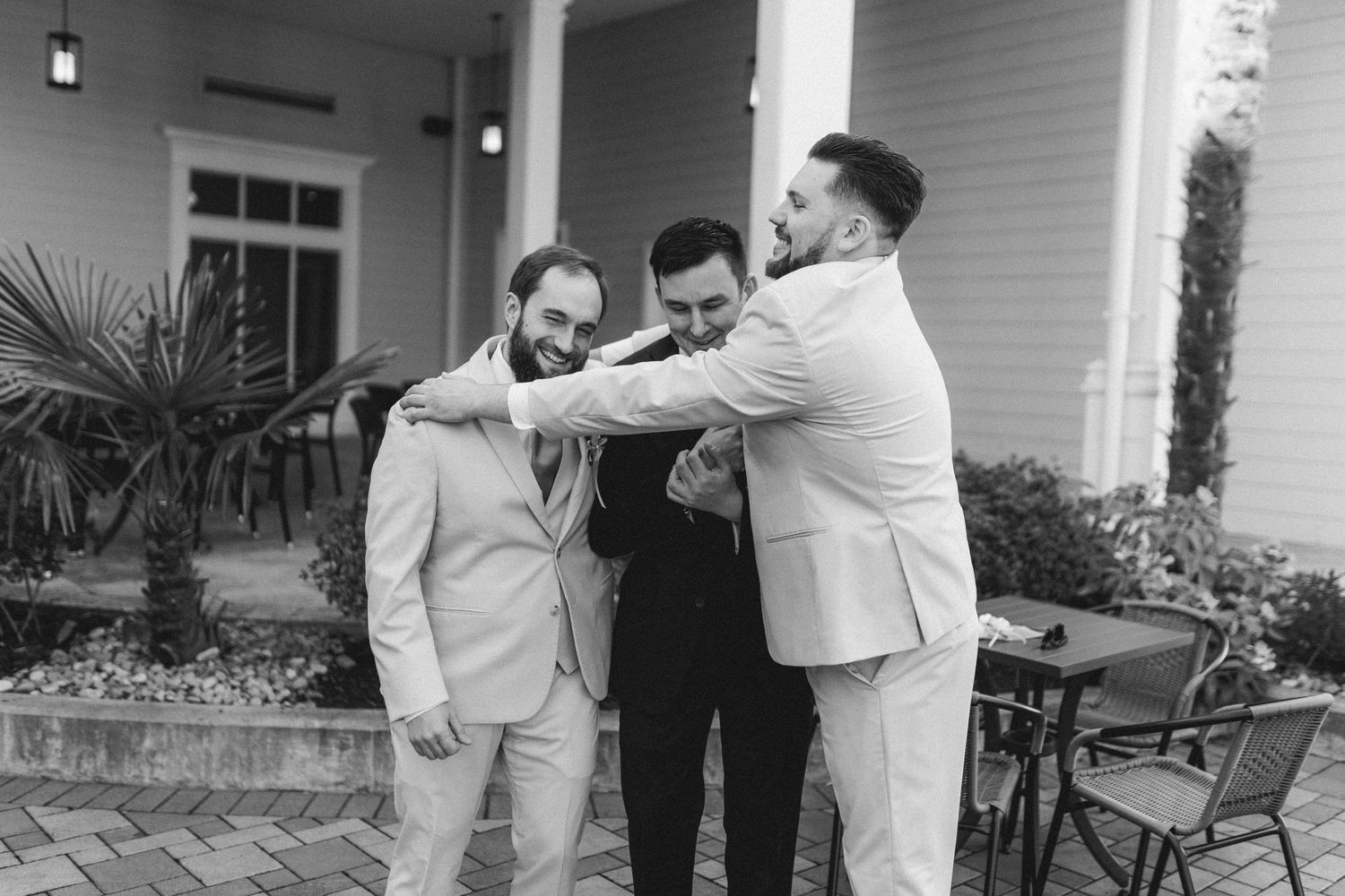 Black and white photo of groomsmen adjusting each others ties outside a wedding venue.