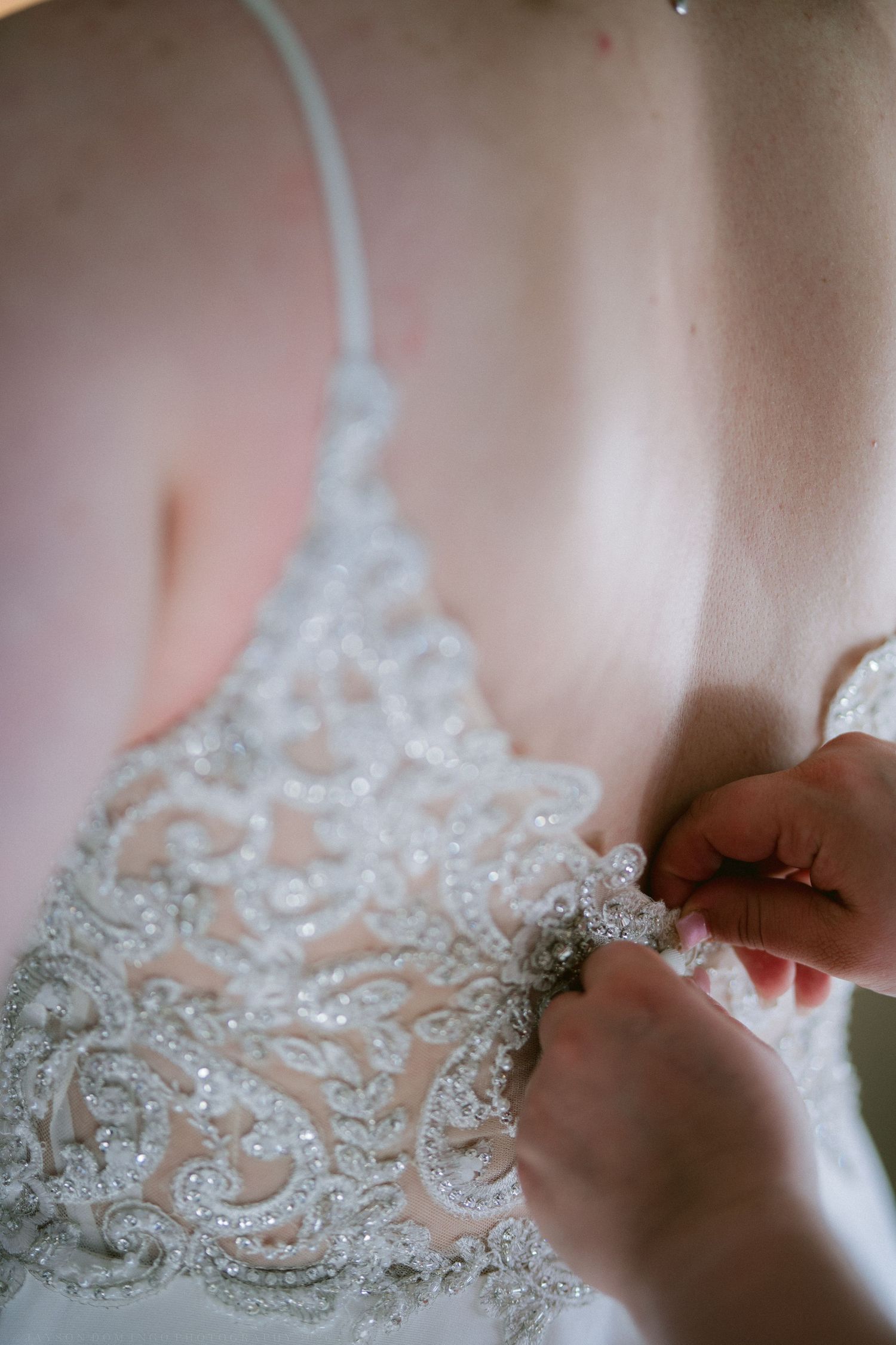 Close-up of hands fastening intricate beaded lace back of elegant bridal wedding gown.