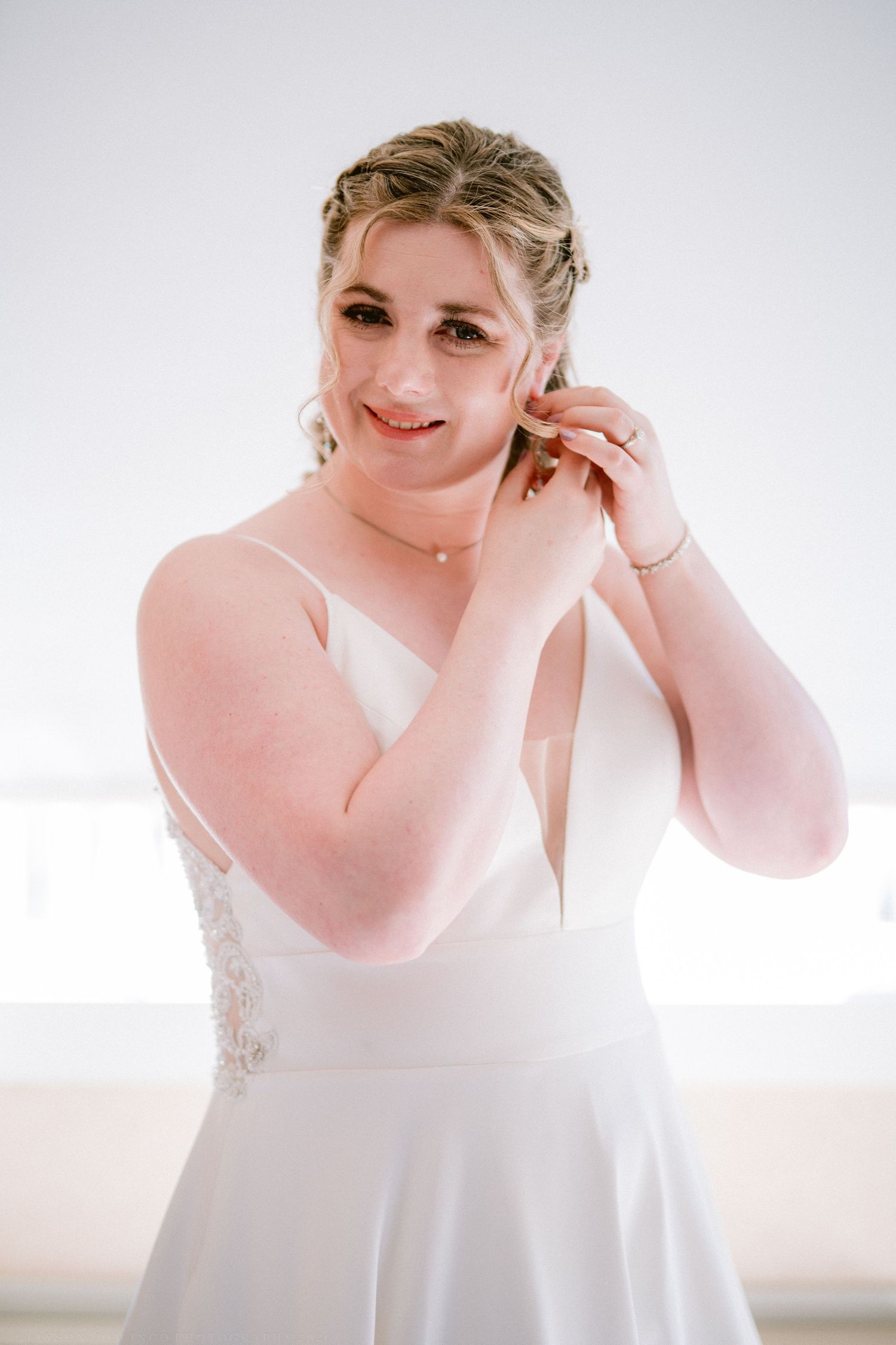 A radiant bride in a white gown puts on earrings while getting ready for her wedding.