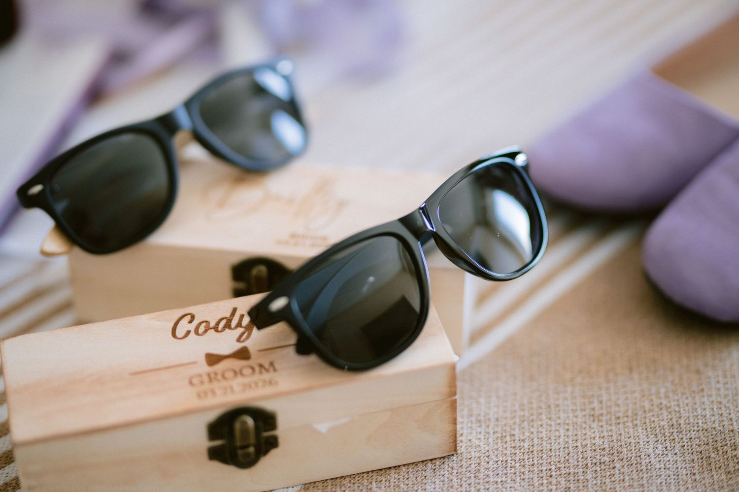 Black wayfarer sunglasses displayed on personalized wooden groom gift boxes at a wedding.