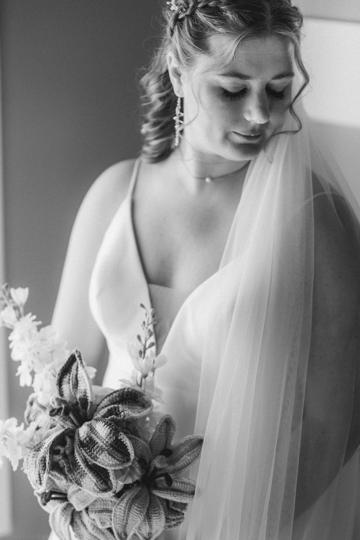 Black and white bridal portrait of a bride in a wedding gown holding a bouquet, wearing a veil and earrings.