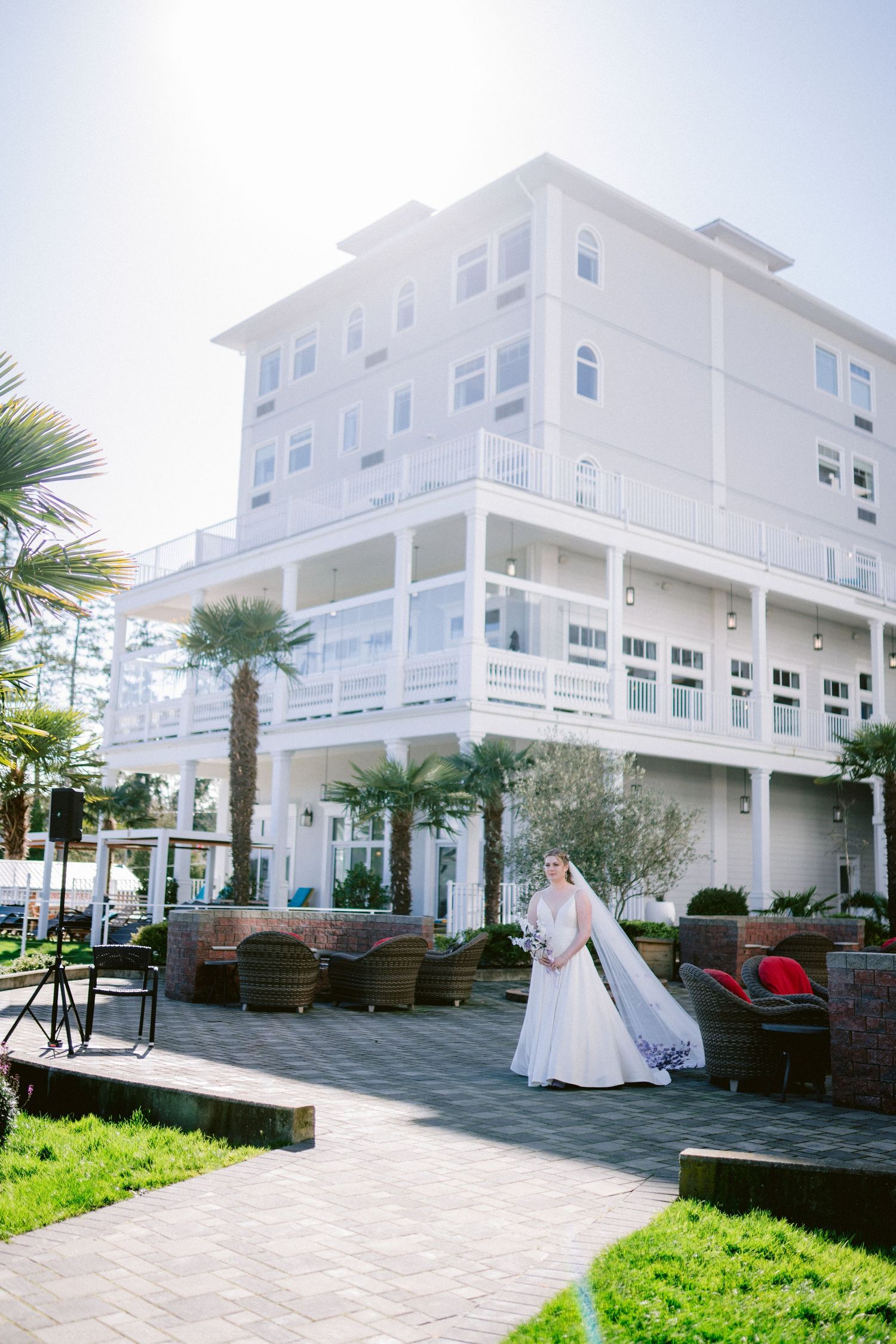 Bride in white gown with long veil posing outside grand white beachside wedding hotel venue.