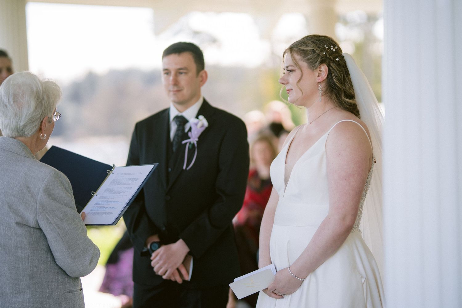 Bride and groom listen to officiant during intimate outdoor wedding ceremony under elegant white gazebo.