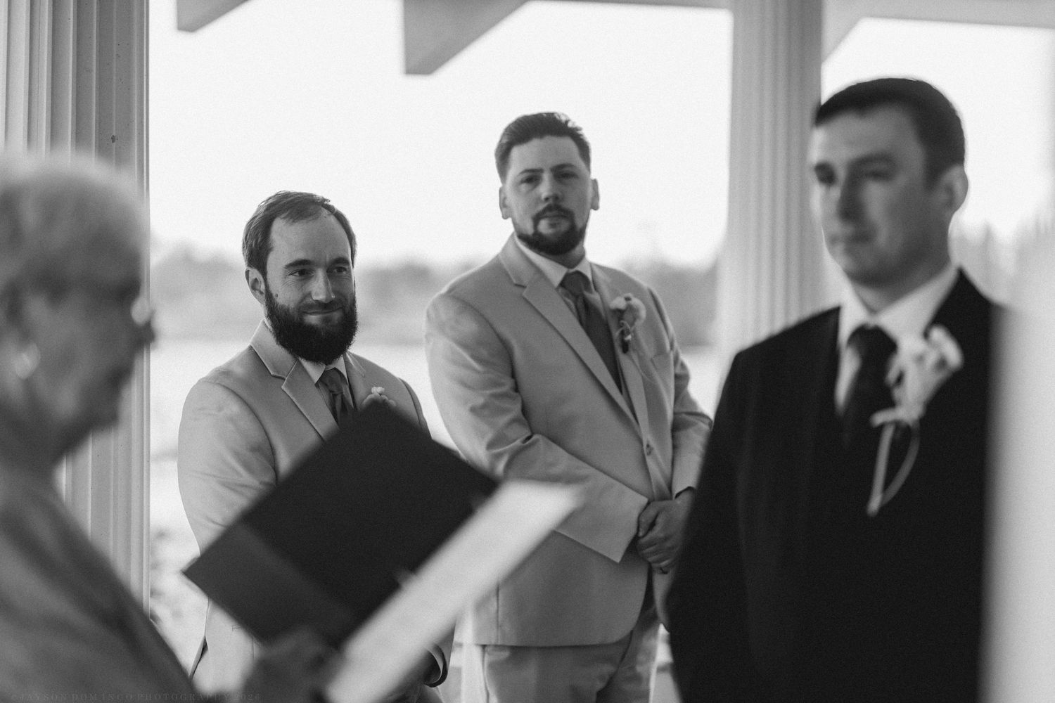 Black and white photo of groomsmen standing attentively during outdoor wedding ceremony at the altar.