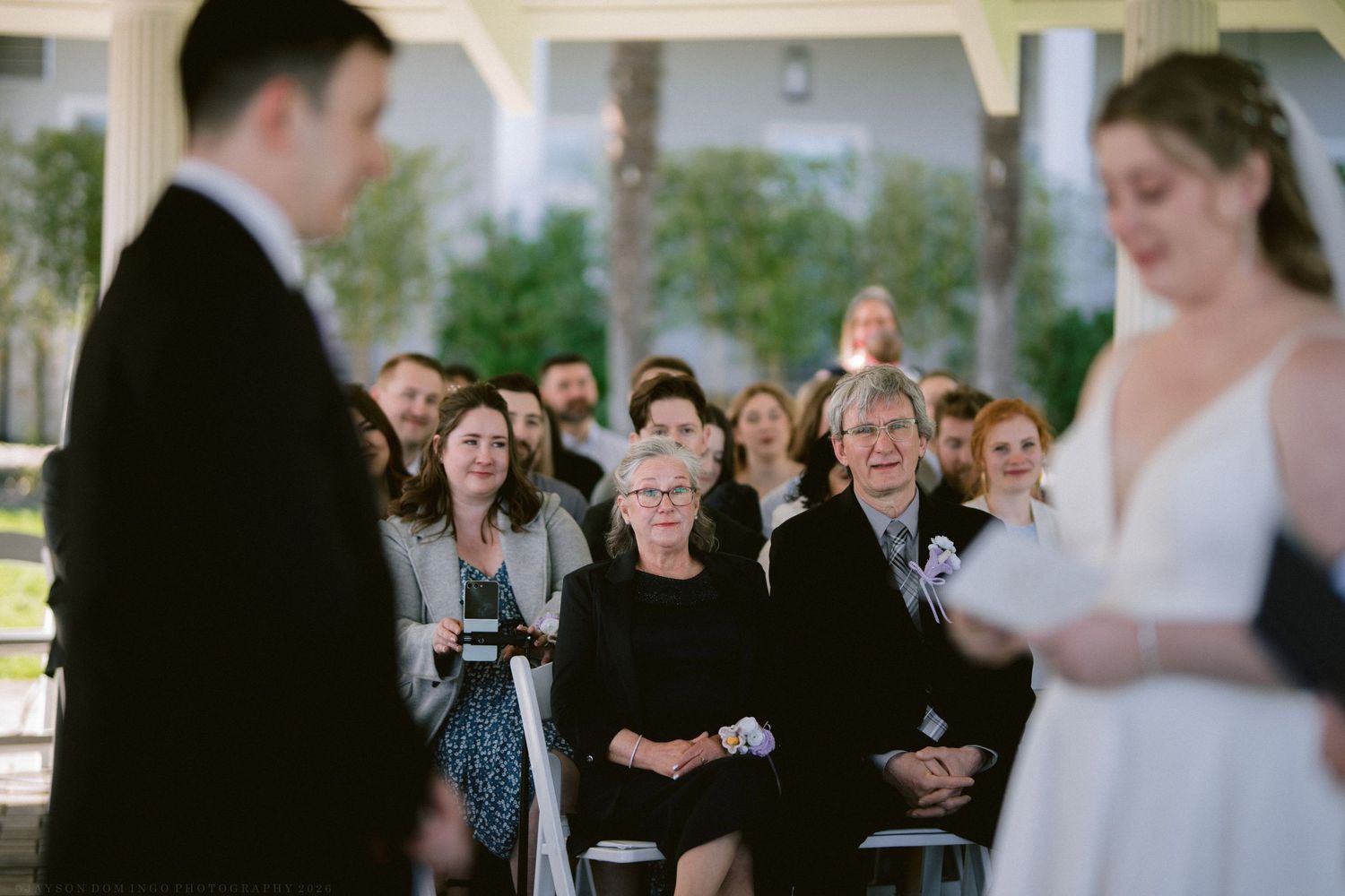 Emotional wedding guests watching bride and groom exchange vows during an elegant outdoor ceremony.